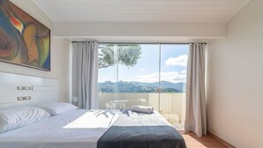 Une chambre à coucher avec un lit, un tableau, une vue sur l’extérieur et une fenêtre avec des rideaux.