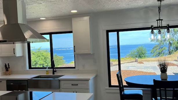 A modern kitchen with a large island, a dining area with a view of the ocean, and a ceiling with a textured finish. - Sweet Caroline Water View (Port Angeles)