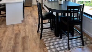 A modern kitchen with white cabinetry, a stainless steel refrigerator, and a dining area with a dark wooden table and chairs. - Sweet Caroline Water View (Port Angeles)