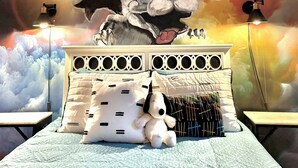 Een slaapkamer met een bed, kussens, een pluchen speelgoed en een muurschildering.
