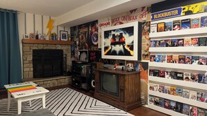 Een woonkamer met een open haard, een televisie, een boekenkast en een muur met filmposters.