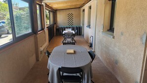 Un patio couvert avec une table ronde et des chaises, donnant sur la rue, et doté d’un sol carrelé.