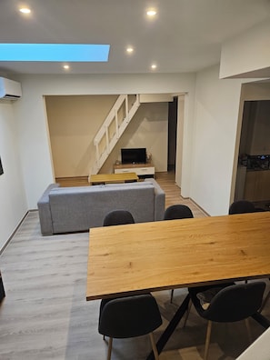 A modern living space with a dining area, a sofa, a TV, and a staircase.