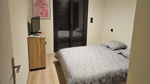 Une chambre à coucher avec un lit, un téléviseur posé sur un meuble en bois, une armoire et une porte avec un miroir.