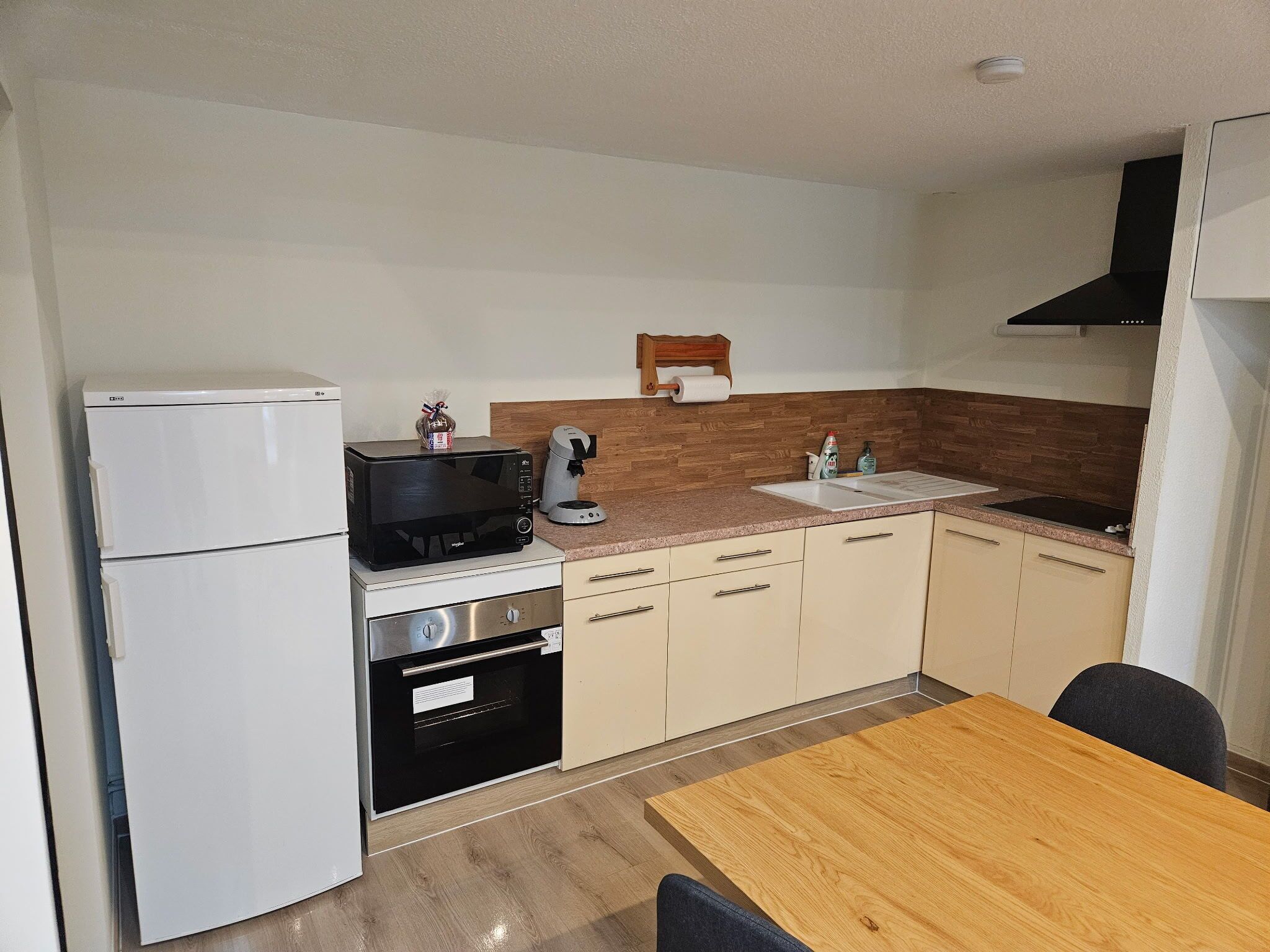 A compact kitchen with a refrigerator, microwave, coffee maker, and a wooden table.
