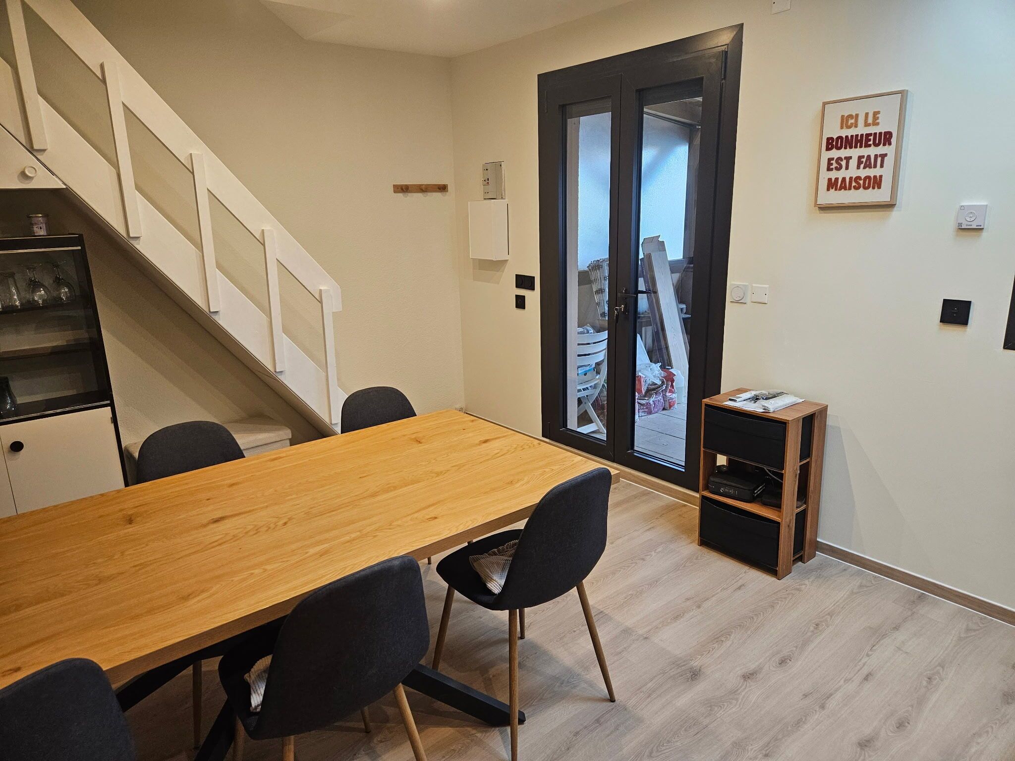Ein Essbereich mit Holztisch und -stühlen, einer Treppe, einer Tür mit Milchglas und einem an der Wand befestigten Schild.