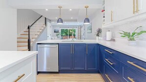 Uma cozinha moderna com armários azul escuro, uma lava-louças de aço inoxidável e iluminação pendente.