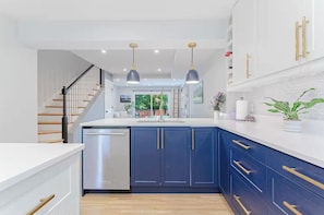 A modern kitchen with dark blue cabinets, a stainless steel dishwasher, and pendant lighting. - Walk to museums and restaurants. Free Parking (Washington)