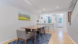 Uma cozinha moderna com armários brancos, uma área de refeições com mesa e cadeiras de madeira, e um tapete azul.