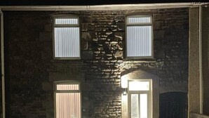 Un edificio in pietra con tre finestre e una porta, illuminato da luci esterne.