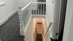 Una scala con finiture in legno e balaustre bianche, che porta a un pianerottolo con pavimento rivestito di moquette.
