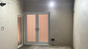 Un cortile stretto con pavimento piastrellato, una porta doppia con persiane verticali e una piccola finestra sopra la porta.