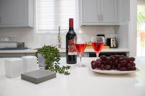 A kitchen counter with a wine bottle, two glasses of red wine, a plate of grapes, a stack of napkins, and a potted plant. - Tangerine Sunsets Blue Marlin (Nassau)