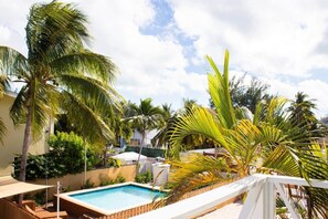 Área de piscina com hidromassagem, cercada por palmeiras e um muro branco.
