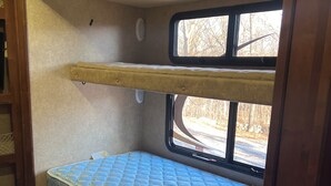 Un intérieur de camping-car compact comprenant un lit superposé, une fenêtre donnant sur l’extérieur et une petite étagère.