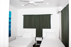 Ein kleines Hotelzimmer für Einzelpersonen mit zwei Betten, einem Deckenventilator, einer Klimaanlage und einem Nachttisch.