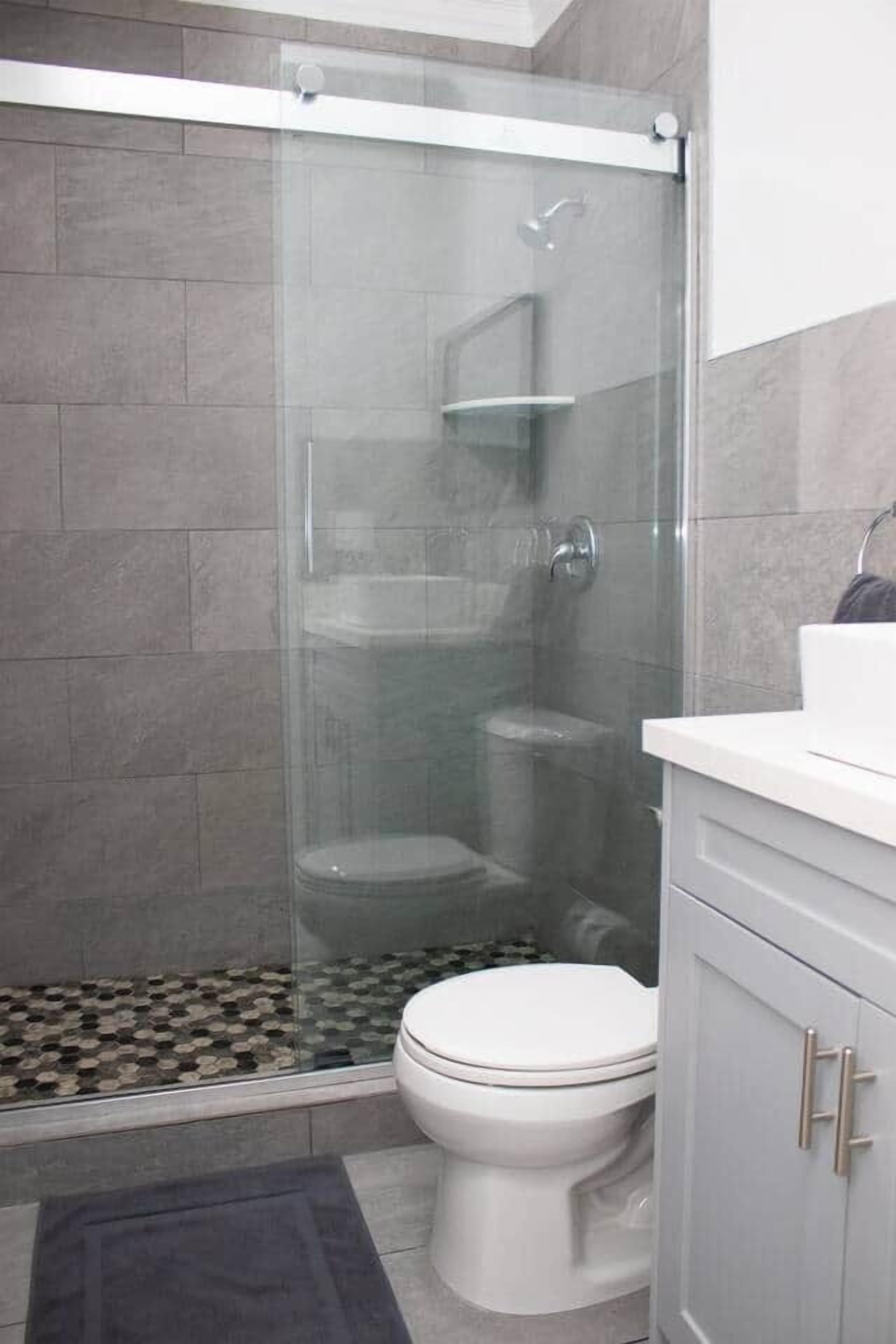 Een moderne badkamer met een douchecabine van glas, een wit toilet en een witte wastafel met zilveren handgrepen.