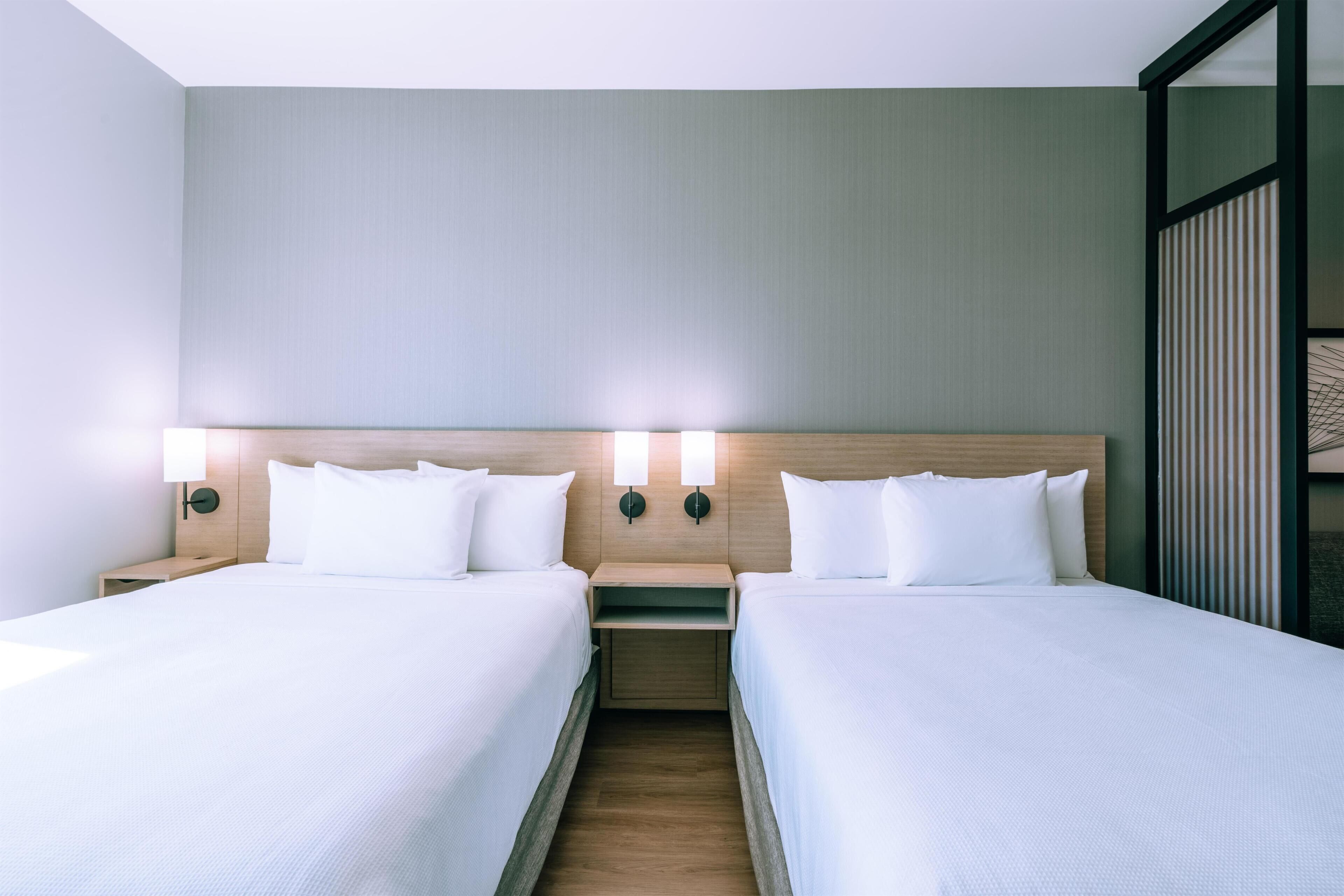 Hotellihuone, jossa on kaksi sänkyä, puinen pääty ja kaksi yöpöytää, joissa on lamput.
