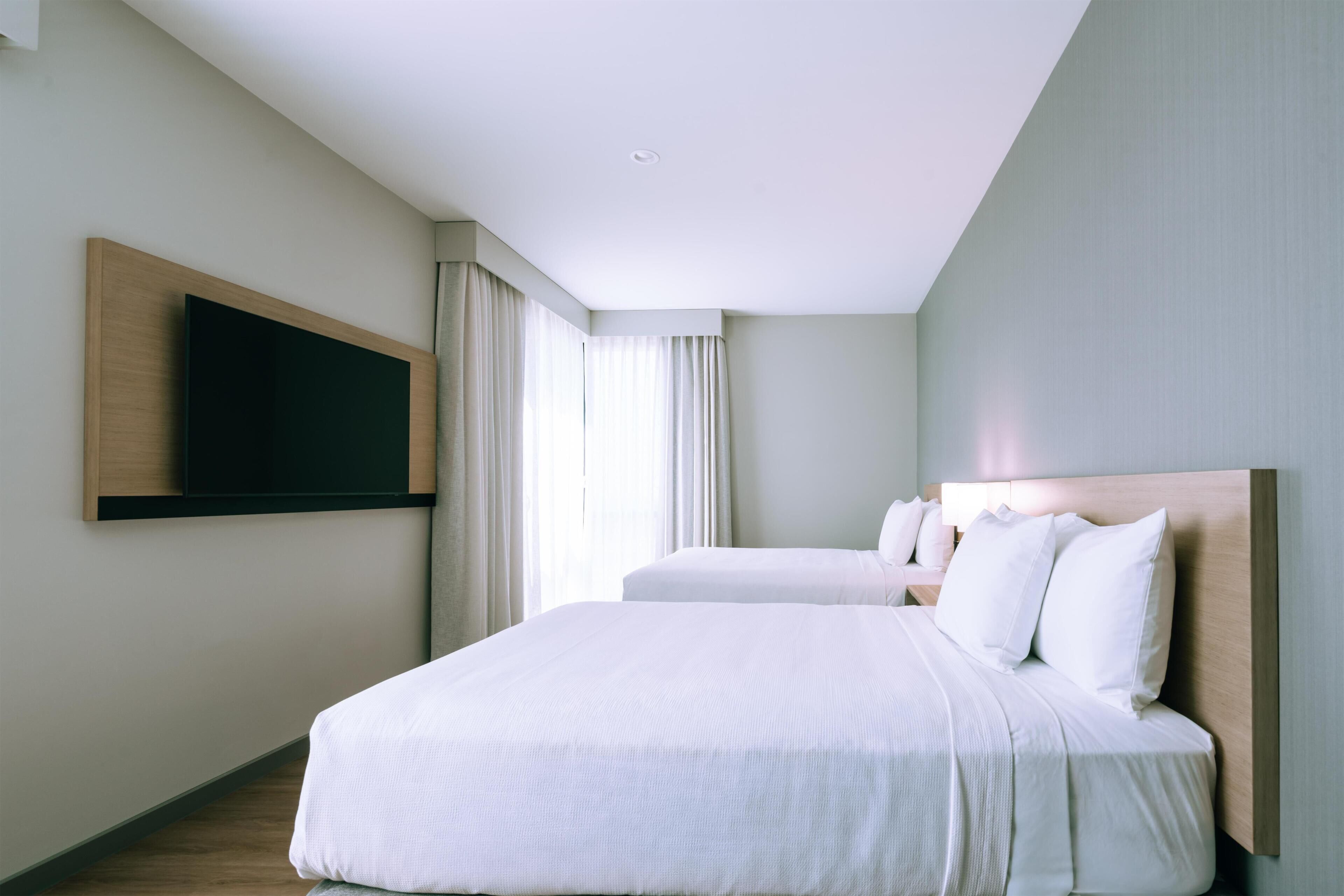 A hotel room with a large bed, a TV mounted on the wall, and a window with curtains.
