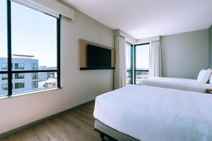 Une chambre d’hôtel avec un grand lit, un téléviseur fixé au mur et une vue sur la ville par la fenêtre.