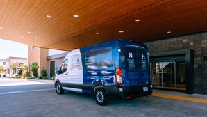 Una camioneta azul estacionada bajo un techo de madera con iluminación empotrada, cerca de la entrada de un edificio.