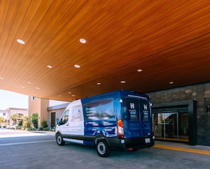 Una camioneta azul estacionada bajo un techo de madera con iluminación empotrada, cerca de la entrada de un edificio.