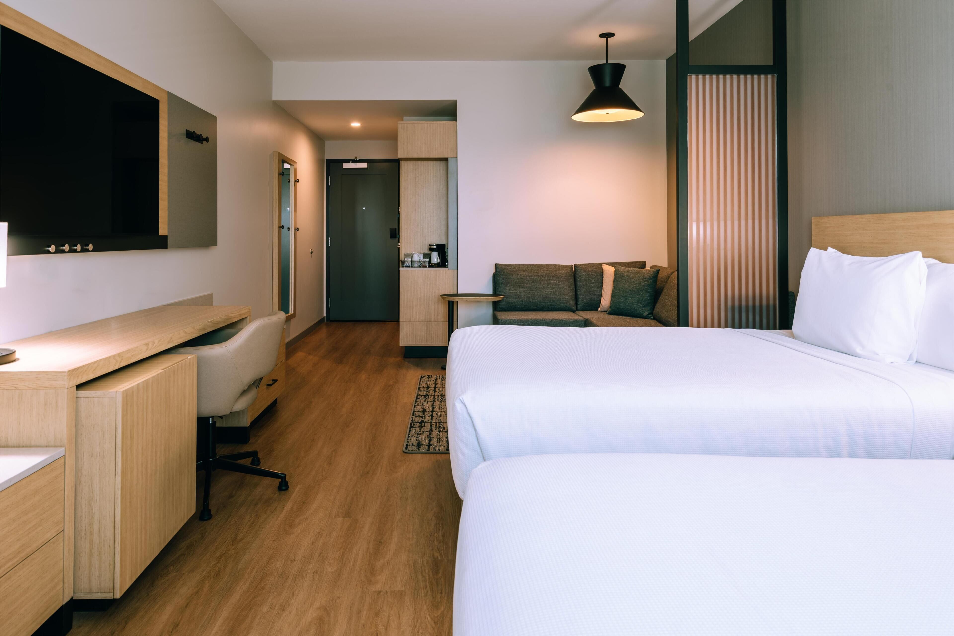 A hotel room with a bed, a desk, a chair, a sofa, and a small table.