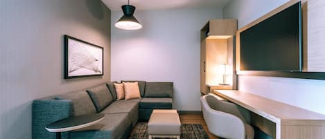 Una sala de estar moderna con un sofá modular, una mesita, un escritorio con una silla, un televisor montado en la pared y un cuadro enmarcado.