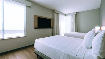 Habitación de hotel con una cama grande, un televisor de pantalla plana en la pared y una ventana con cortinas.
