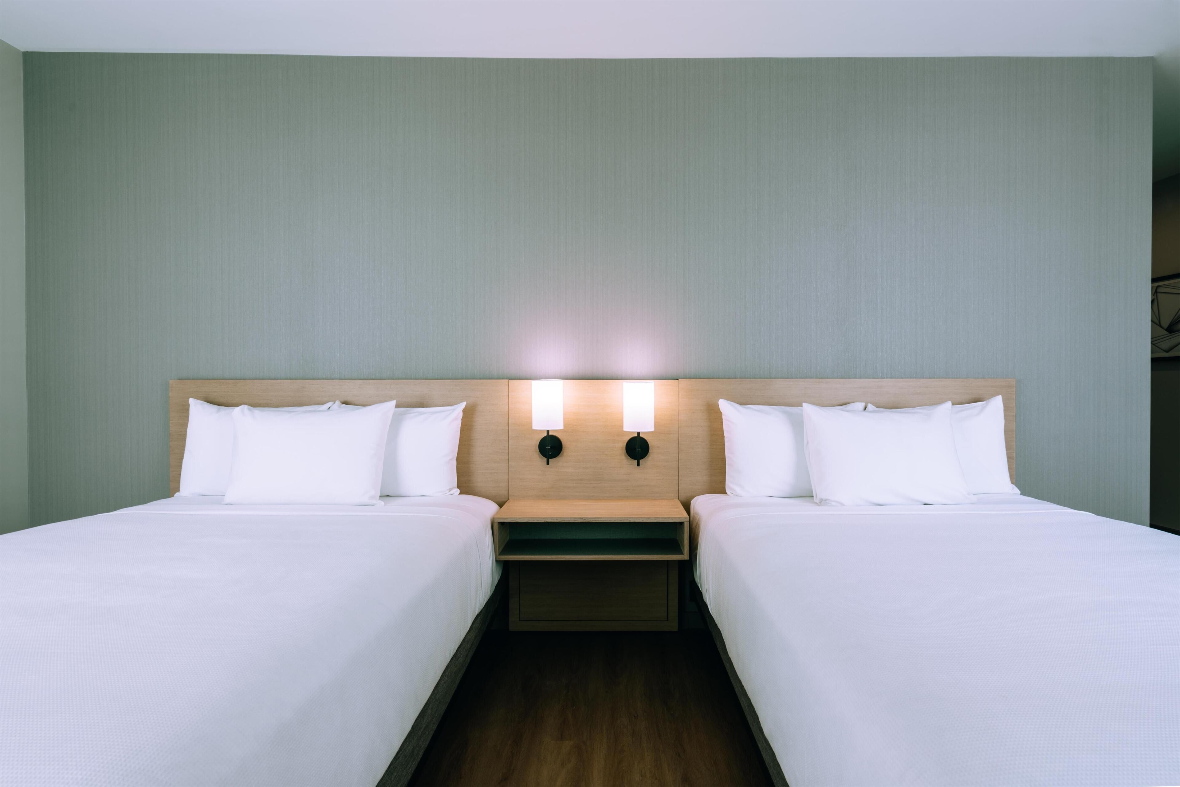 A hotel room with two beds, a wooden headboard, and a nightstand with a lamp.