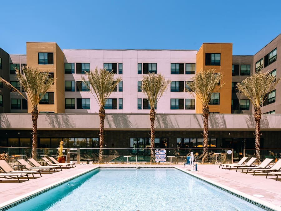 Ein Hotel mit Swimmingpool, Palmen und einer modernen Fassade.