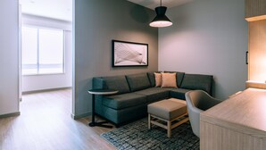 Una sala de estar moderna con un sofá modular, una mesita, un sillón, una obra de arte enmarcada y una lámpara colgante.