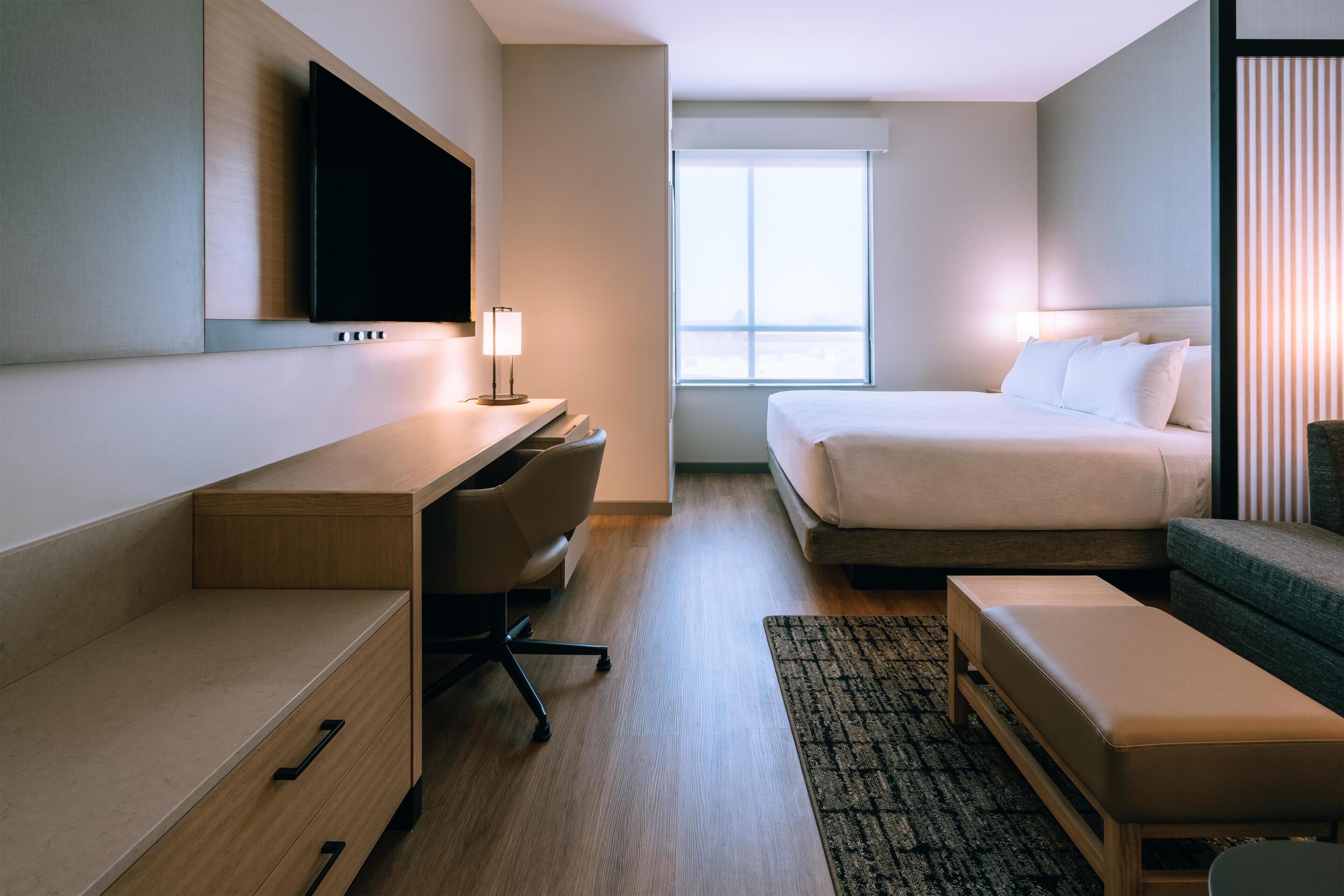 A hotel room with a bed, desk, chair, and a television mounted on the wall.