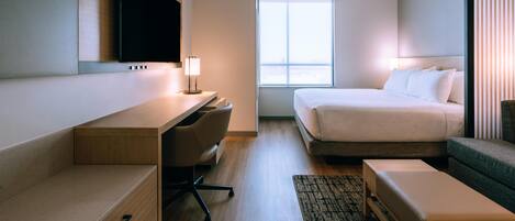 A hotel room with a bed, desk, chair, and a television mounted on the wall.