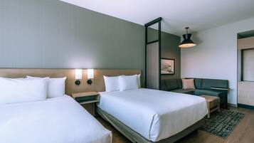 A hotel room with two beds, a nightstand, a seating area with a sofa, and a wall-mounted lamp.