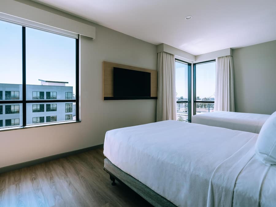Una camera d'albergo con un'ampia finestra, un letto, una TV a schermo piatto fissata al muro e vista su un edificio.