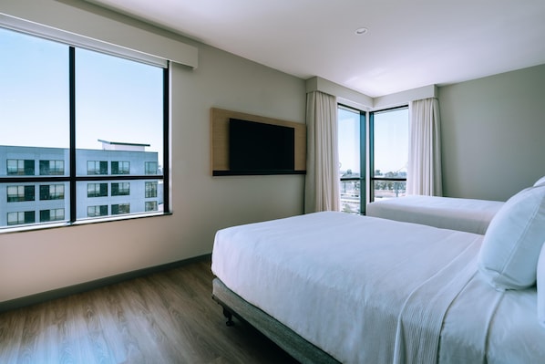 A hotel room with a large window, a bed, a flat-screen TV mounted on the wall, and a view of a building outside. - Hyatt Place Ontario Airport (Ontario)