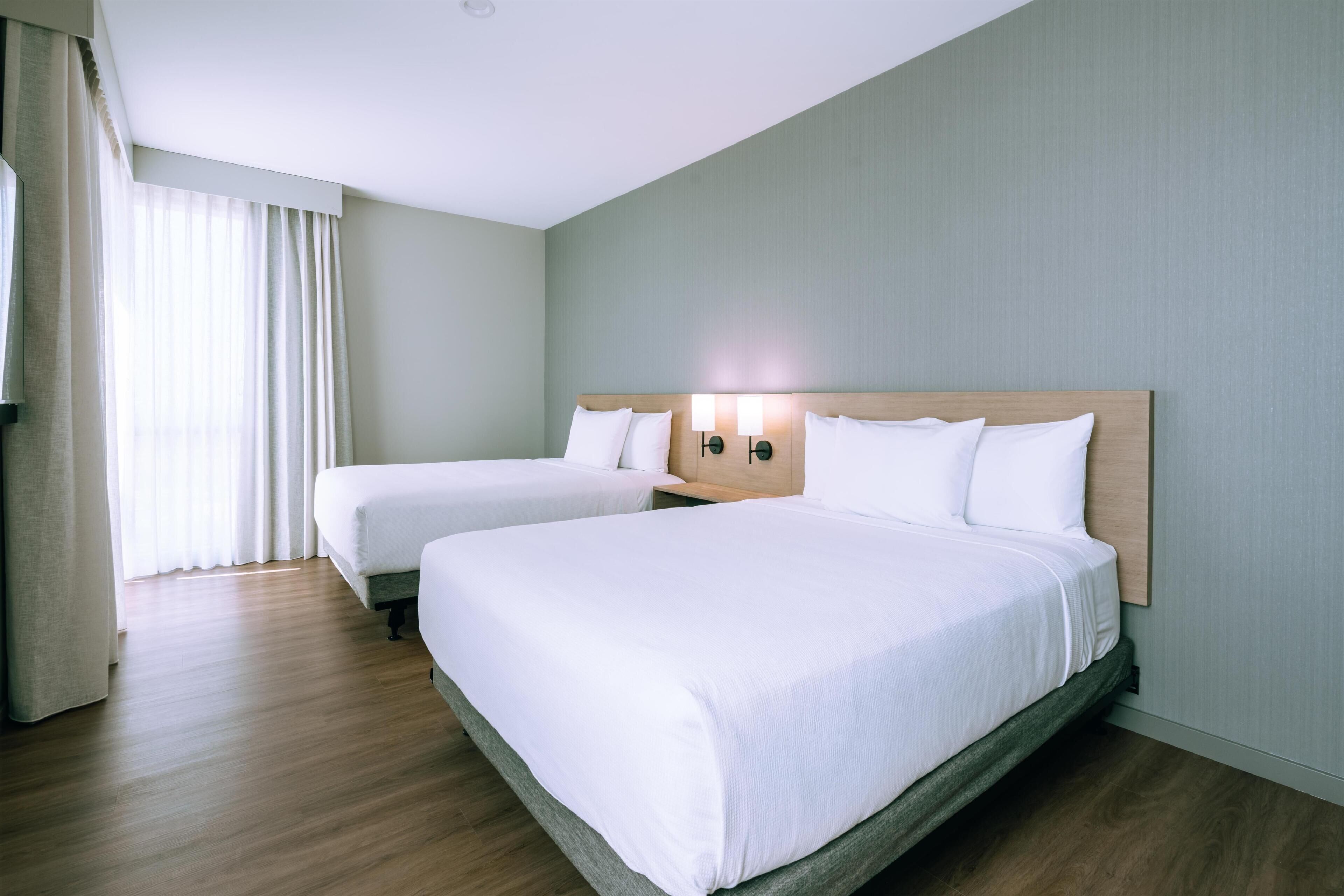 Une chambre d’hôtel avec deux lits simples, une tête de lit en bois et une table de chevet avec des lampes.