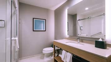 A modern bathroom with a glass shower enclosure, a toilet, a sink with a mirror, and a framed artwork on the wall.