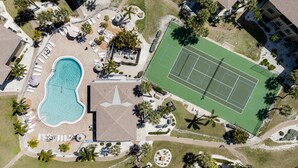 Vista aerea di un resort con piscina, campi da tennis e palme.