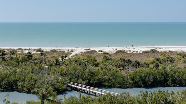 A coastal landscape with a beach, a bridge over water, and dense greenery. - Gorgeous 2 Story Villa at Blind Pass Condos (Sanibel)
