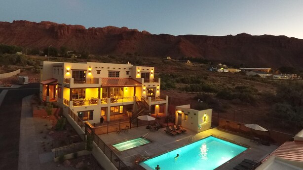A modern two-story hotel with a swimming pool, outdoor seating, and a view of the surrounding landscape.
