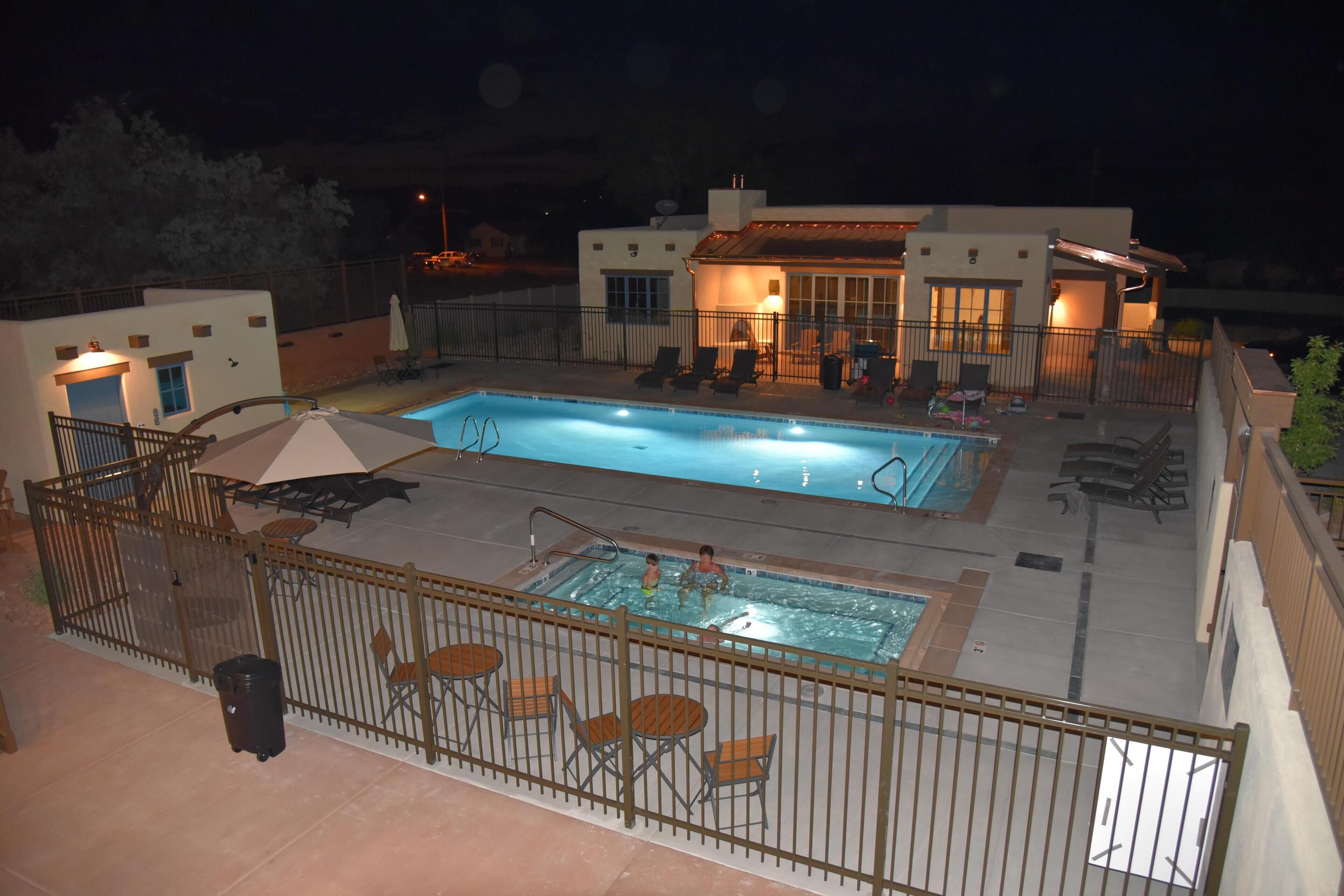 A rooftop pool area with a fenced swimming pool, lounge chairs, and a covered seating area.