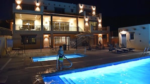 A multi-story hotel with a swimming pool, outdoor seating, and a well-lit facade.