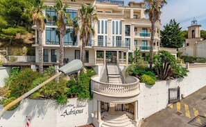 A multi-story hotel with a grand entrance, palm trees, and a staircase leading to the main building. - Le Top du top (Carry-le-Rouet)