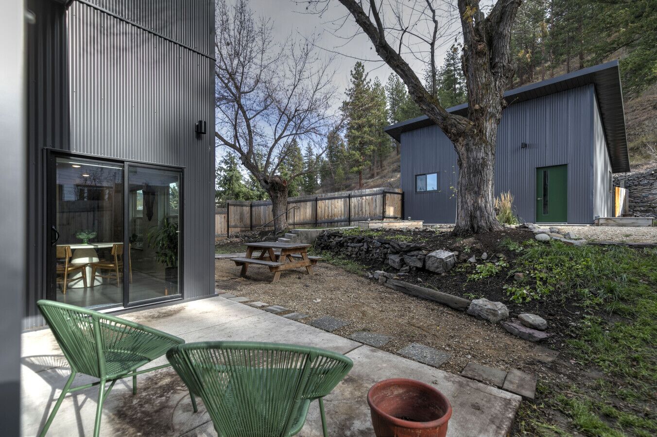 A modern house with a patio area featuring two green chairs and a wooden table.