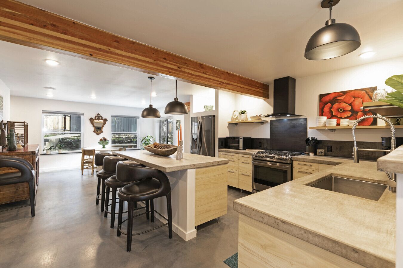 A modern kitchen with a central island, bar stools, and a large window providing natural light.