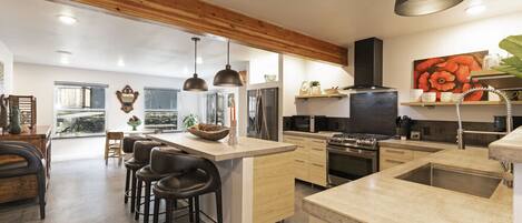 A modern kitchen with a central island, bar stools, and a large window providing natural light.