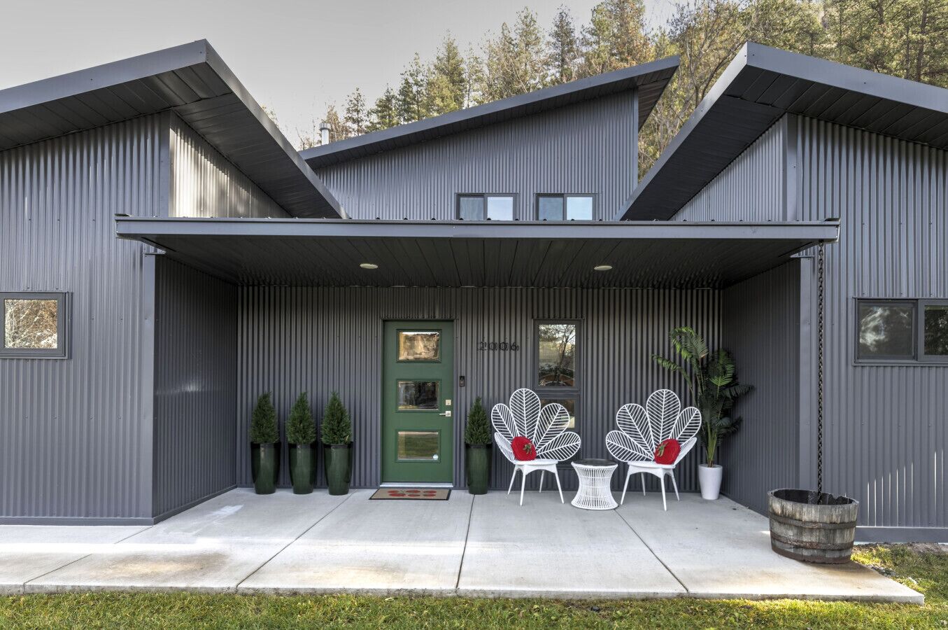A modern building with a grey facade, a green door, and two white chairs with red cushions in front.
