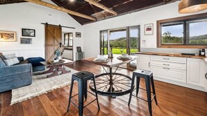 A spacious kitchen with a large window, wooden flooring, and a rustic ceiling. - The Hitching Rail Hut - Relax, Unwind & Reconnect (Coramba)